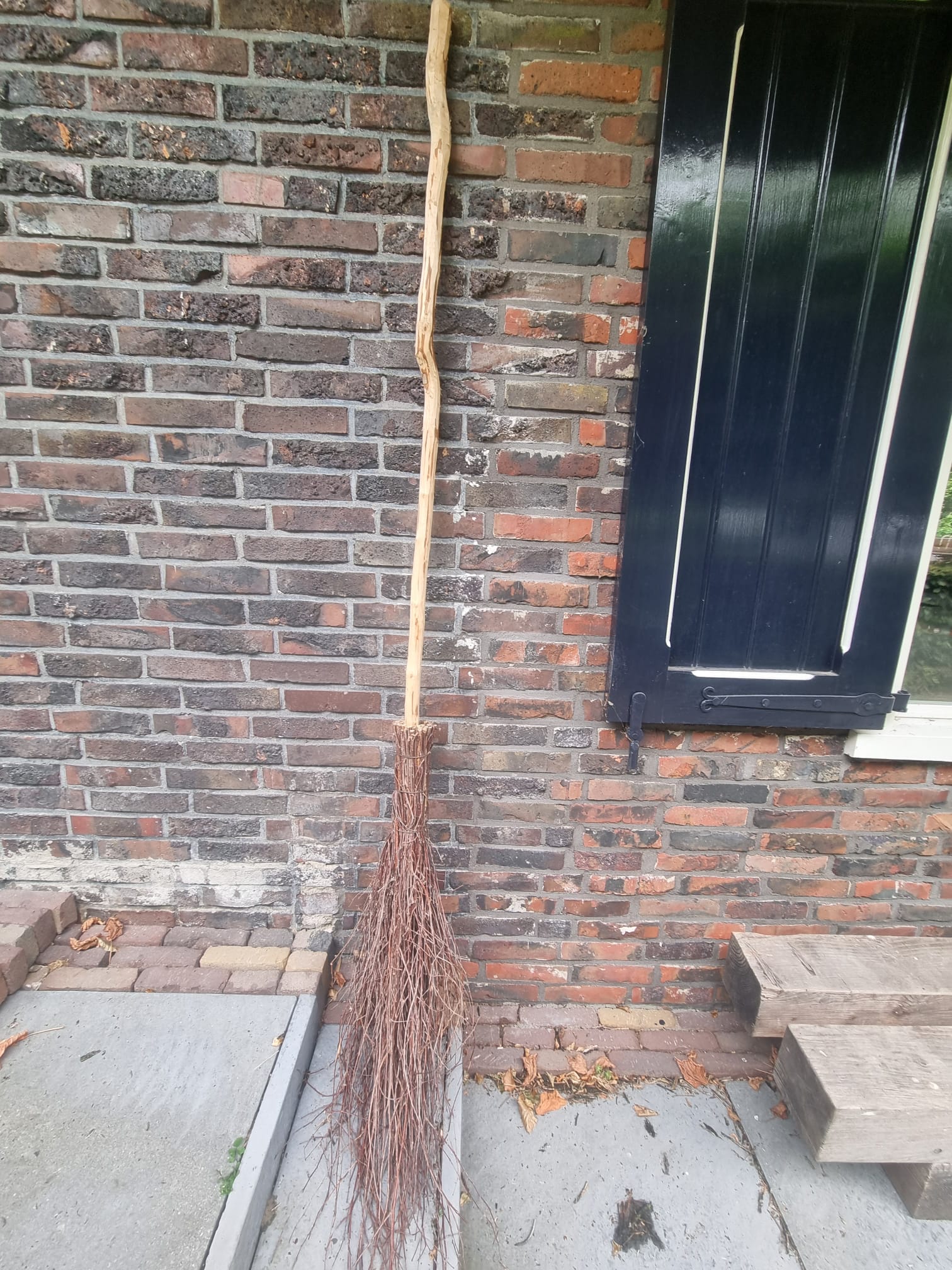 Handgemaakte Drentse berkenbezem met lange houten steel natuurproduct tegen muur geplaatst.